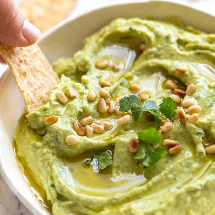 Avocado Dip in a rustic white bowl being scooped up with a corn chip