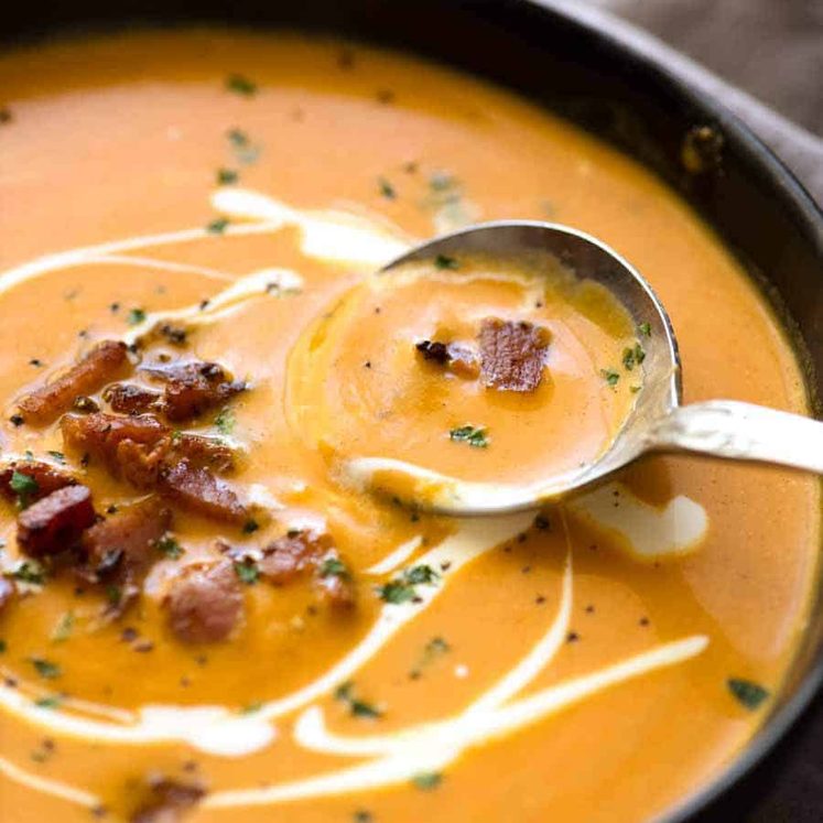 Close up of Carrot Soup in a rustic black bowl being scooped up with a spoon.