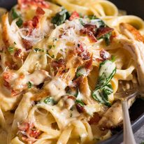 Close up of chicken pasta with creamy alfredo sauce, sun dried tomato, spinach and bacon