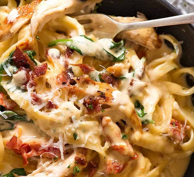 Close up of Chicken Pasta recipe with creamy alfredo sauce, sun dried tomato, spinach and bacon in a rustic black bowl, ready to be eaten