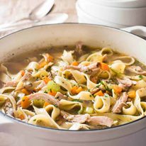 An easy Chicken Noodle Soup in a white cast iron pot, piping hot fresh off the stove.