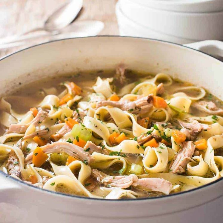 An easy Chicken Noodle Soup in a white cast iron pot, piping hot fresh off the stove.