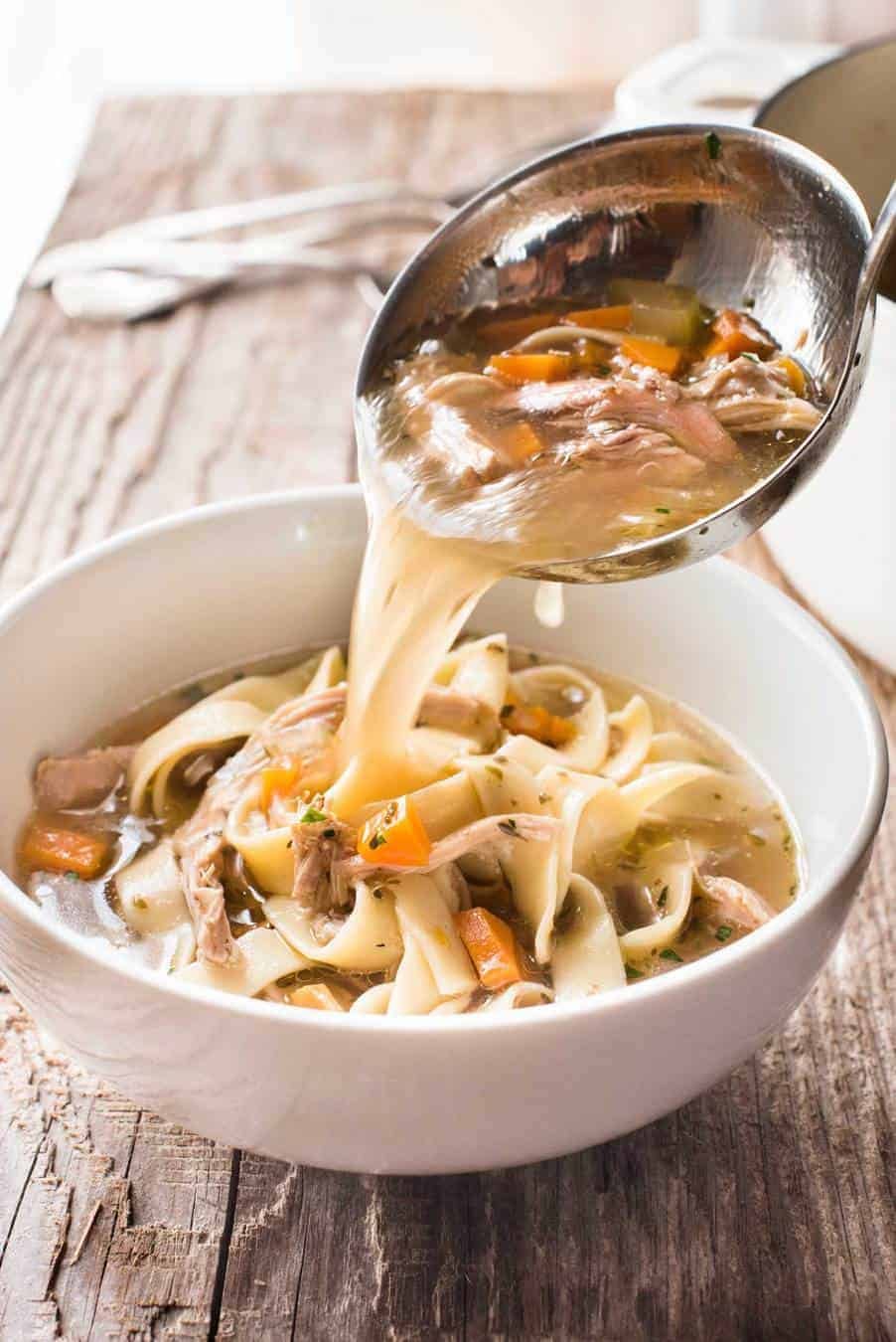 Chicken Vegetable Noodle Soup broth being poured into a bowl with a soup ladle.