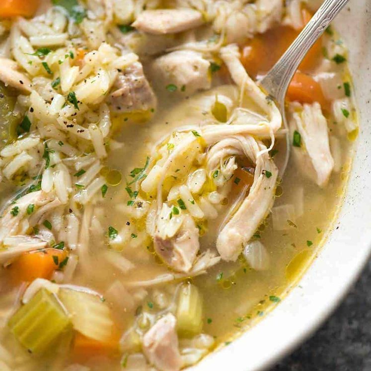 Close up of chicken and rice soup in a rustic beige bowl, ready to be eaten.