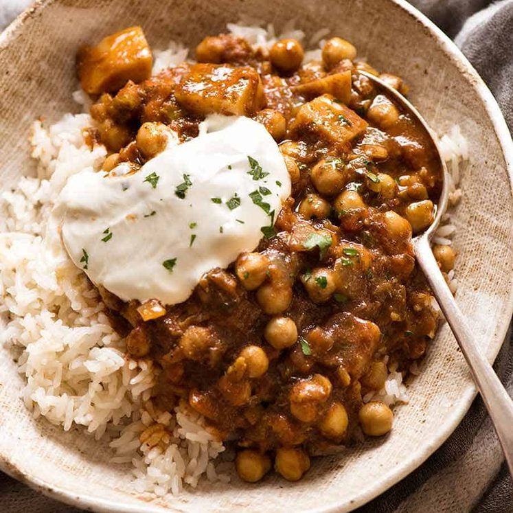 Photo of Chickpea Curry (Chana Aloo) in a bowl over coconut rice with a dollop of yogurt in a rustic bowl, ready to be eaten