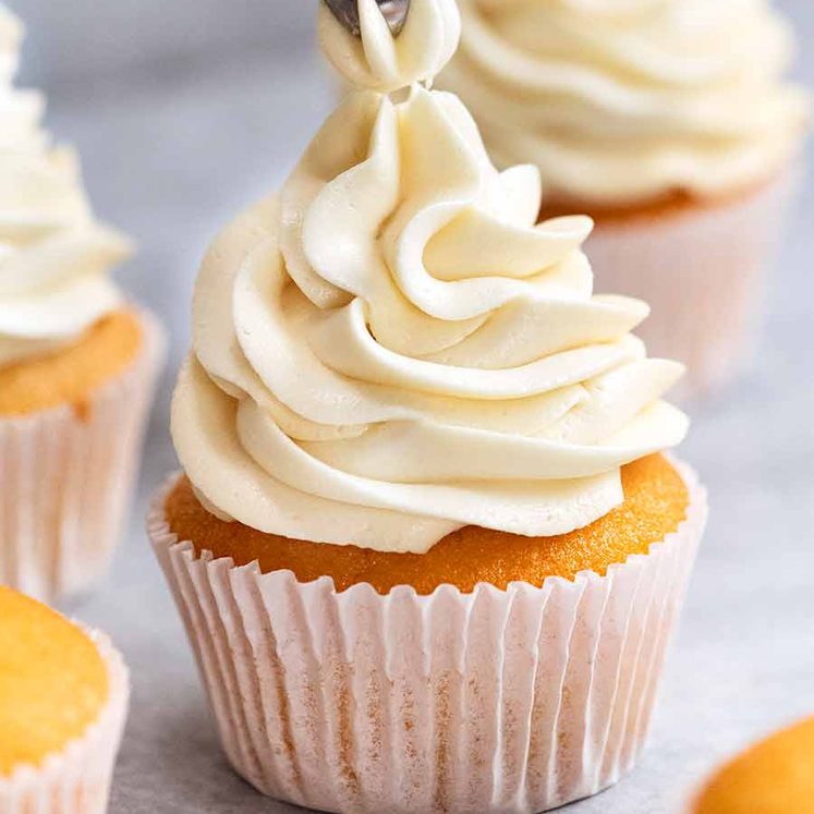 Close up piping Fluffy Vanilla Frosting onto Vanilla Cupcake