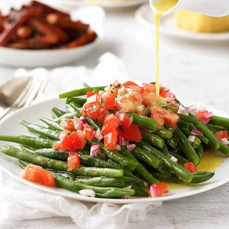 Pouring lemon dressing over green bean salad