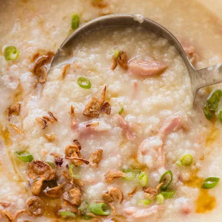 Chinese Ham Bone Rice Soup (Congee) being ladled out of a white pot, fresh off the stove