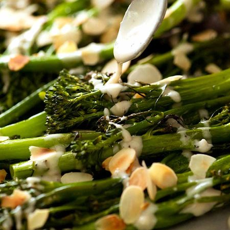 Drizzling tahini sauce over roasted broccolini