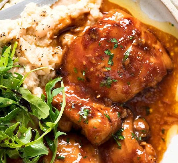 Overhead photo of Sticky Baked Chicken Thighs on a plate with a side of mashed white beans and rocket parmesan salad