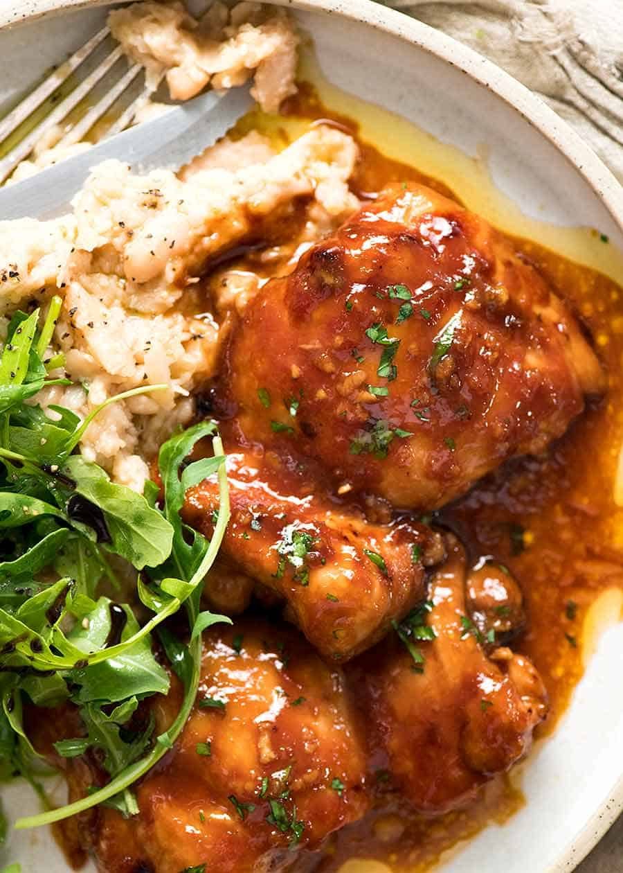 Overhead photo of Sticky Baked Chicken Thighs on a plate with a side of mashed white beans and rocket parmesan salad