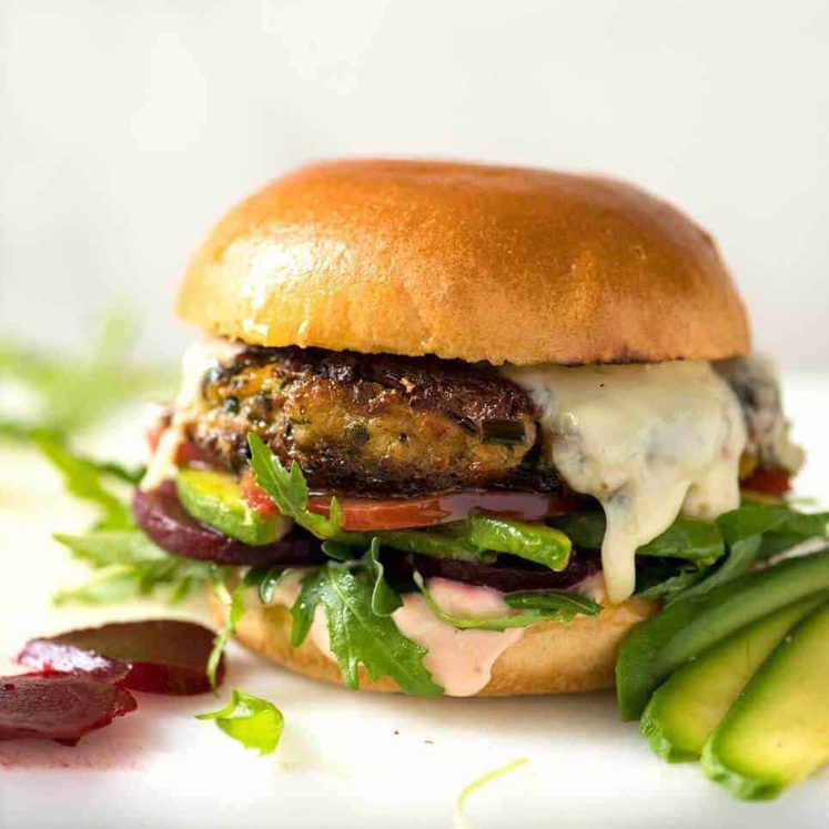 A veggie burger with melted cheese, avocado, beetroot, tomato and lettuce on a soft golden bun.